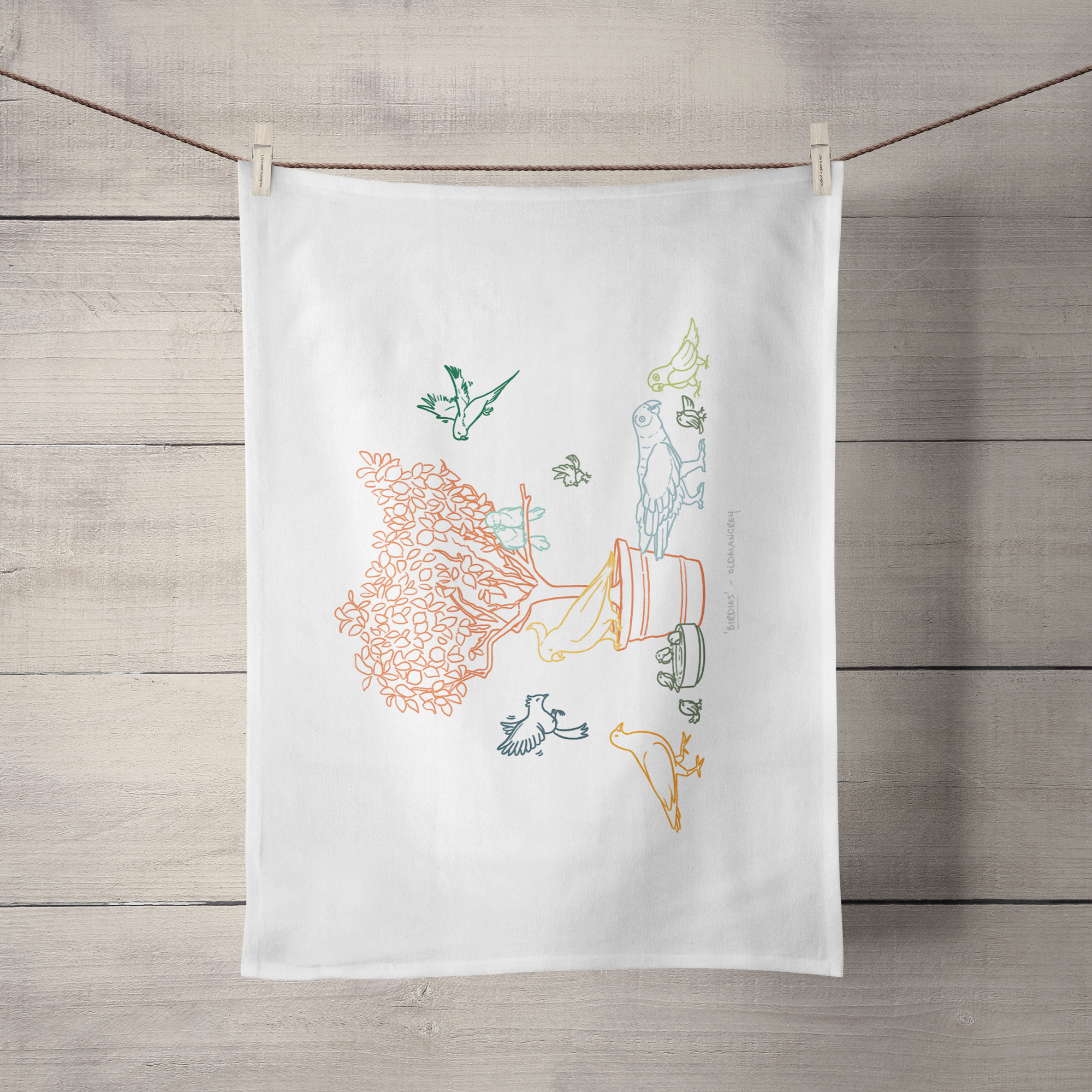 A large tea towel hanging by its short side from a piece of string. It has a colourful digital illustration of birds on & around a small tree.