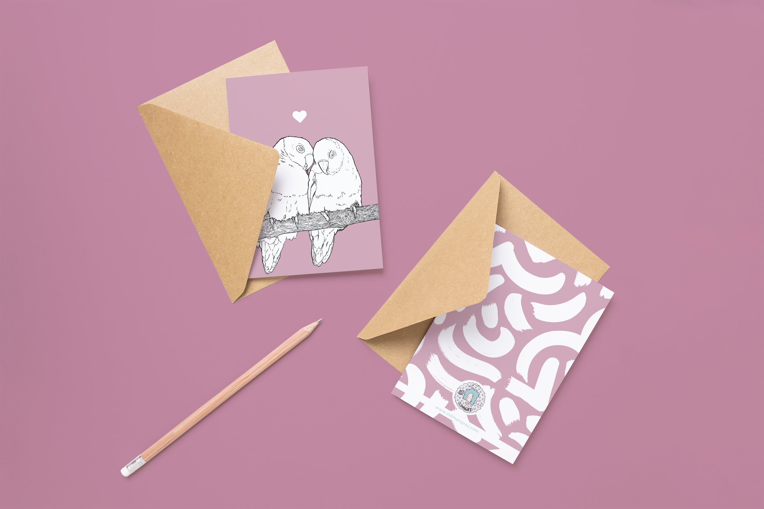 Two cards on brown envelopes, one face up one down. The card and image have a lilac background, with a black & white digital illustration of 2 Lovebirds on a branch.