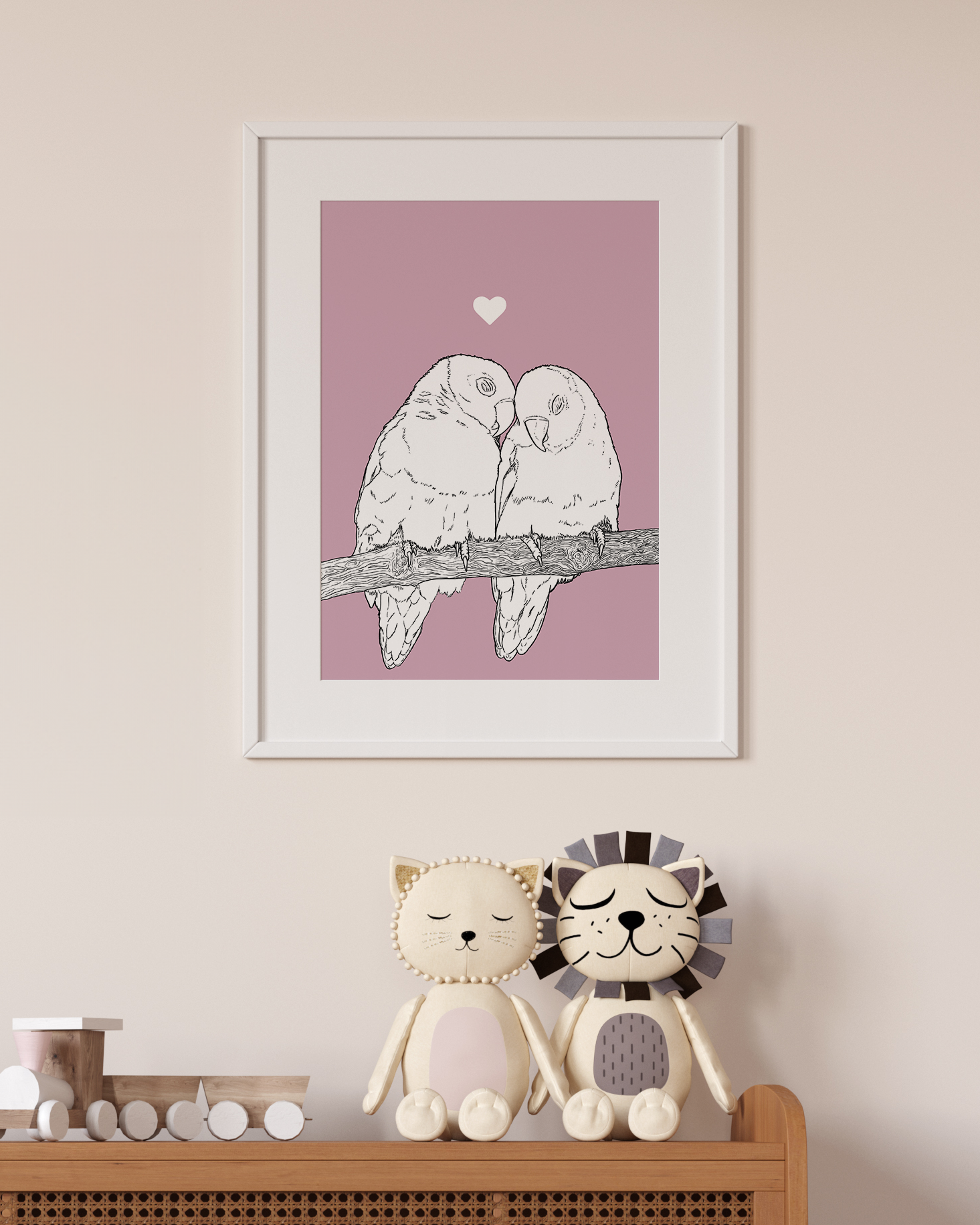An A4 print in a white frame on a wall above 2 lion toys sitting on a unit. It has a black & white illustration of Lovebirds on a pink background.