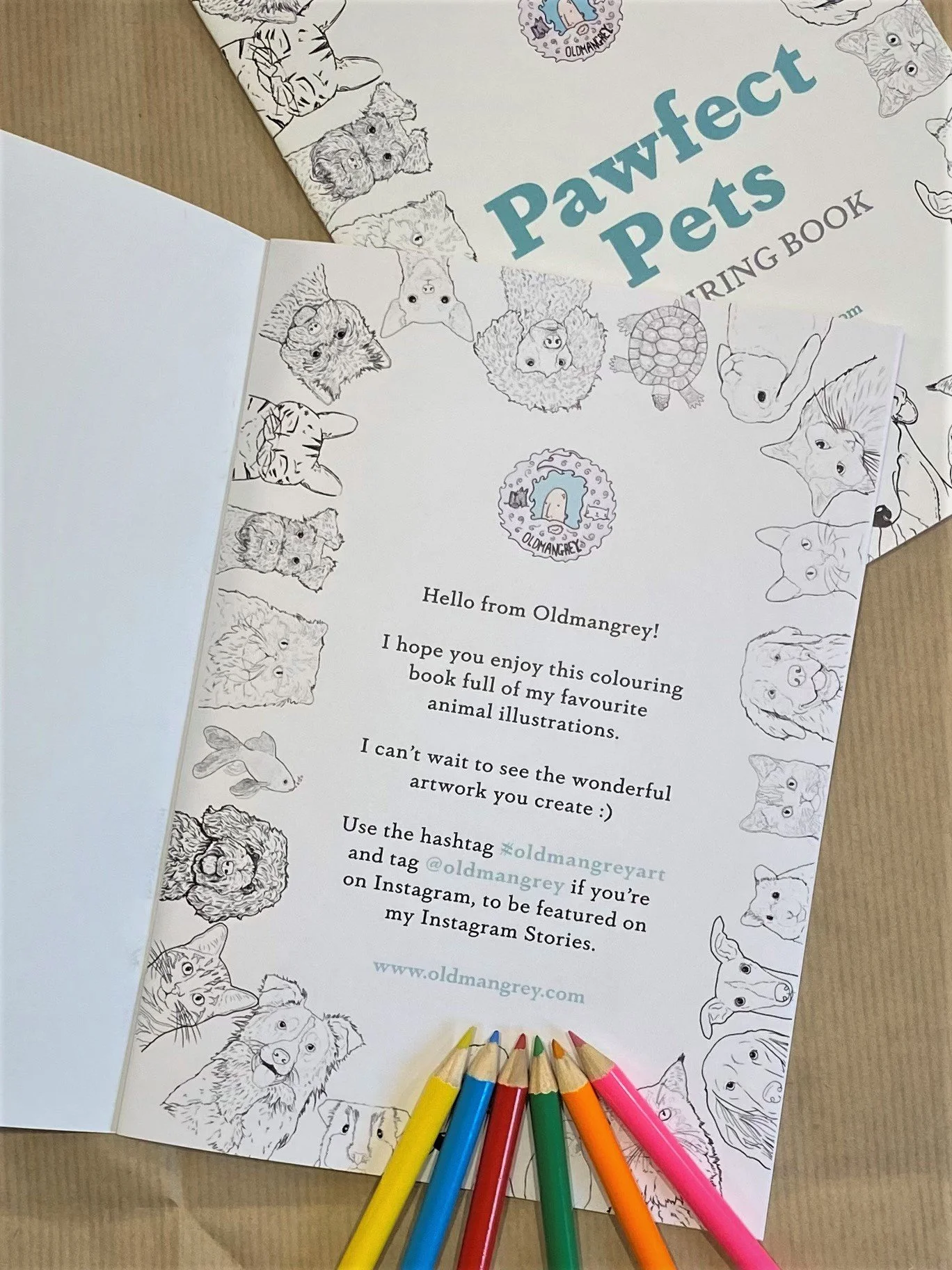 The first inside page of my A5 Pawfect Pets colouring book, lying on fanned out copies, with mini colouring pencils scattered around.