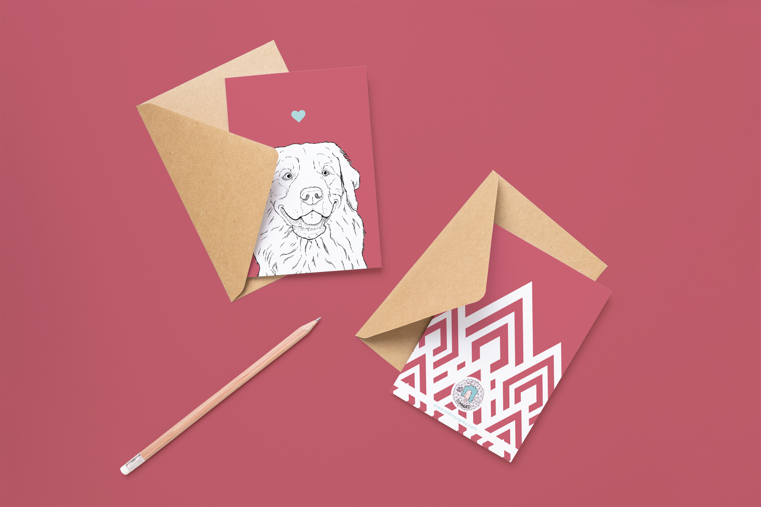 Two cards on brown envelopes, 1 face up 1 down. The card and image have a purple red coloured background, with a black & white digital illustration of the head & shoulders of a Golden Retriever dog.
