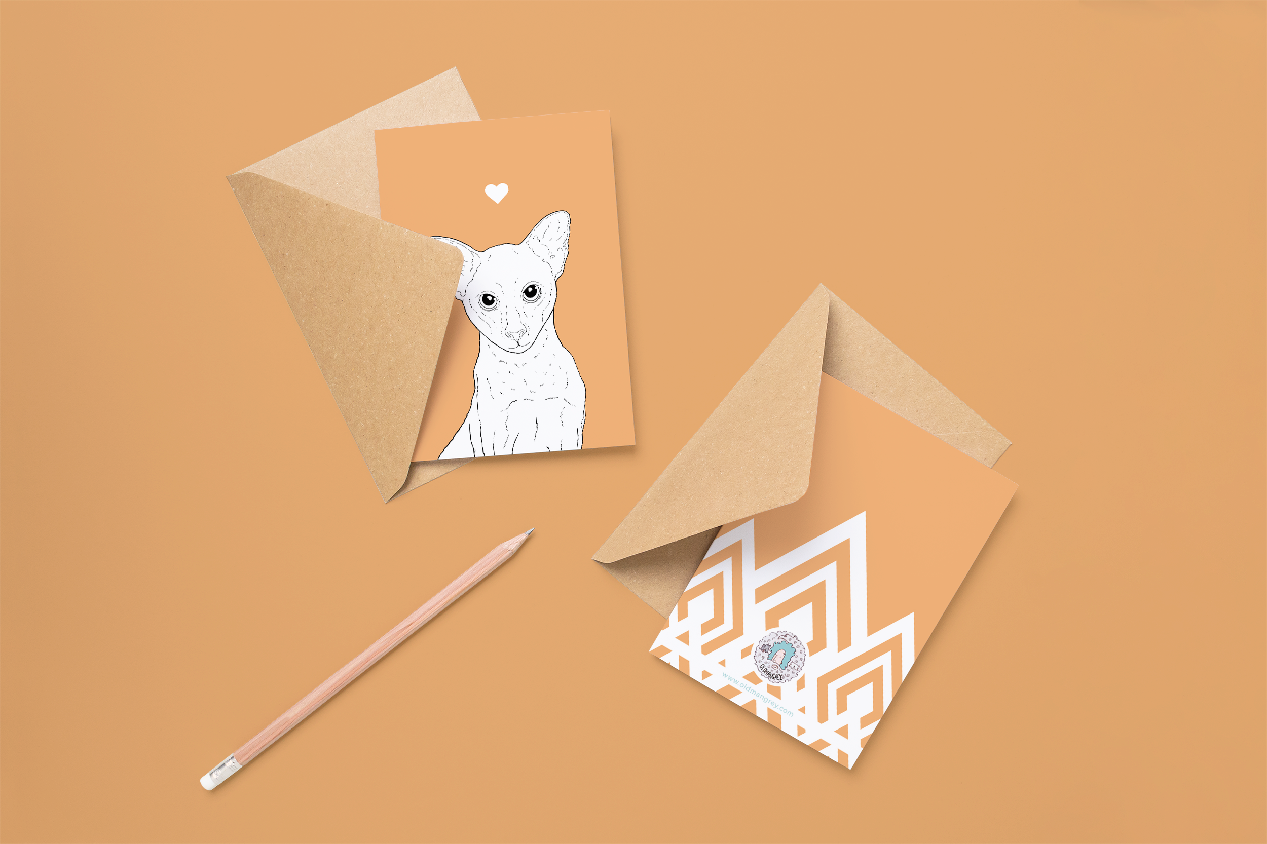 Two cards on brown envelopes, one face up one down. The card and image have a soft orange coloured background, with a black & white digital illustration of the head & shoulders of an Oriental cat.