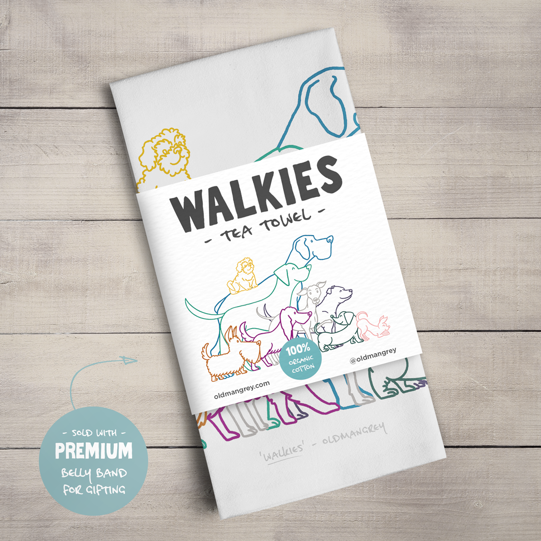 A large tea towel folded to a rectangle wrapped in a paper belly band. This shows the colourful digital illustration of 9 dogs eager for 'Walkies' as shown on the title.