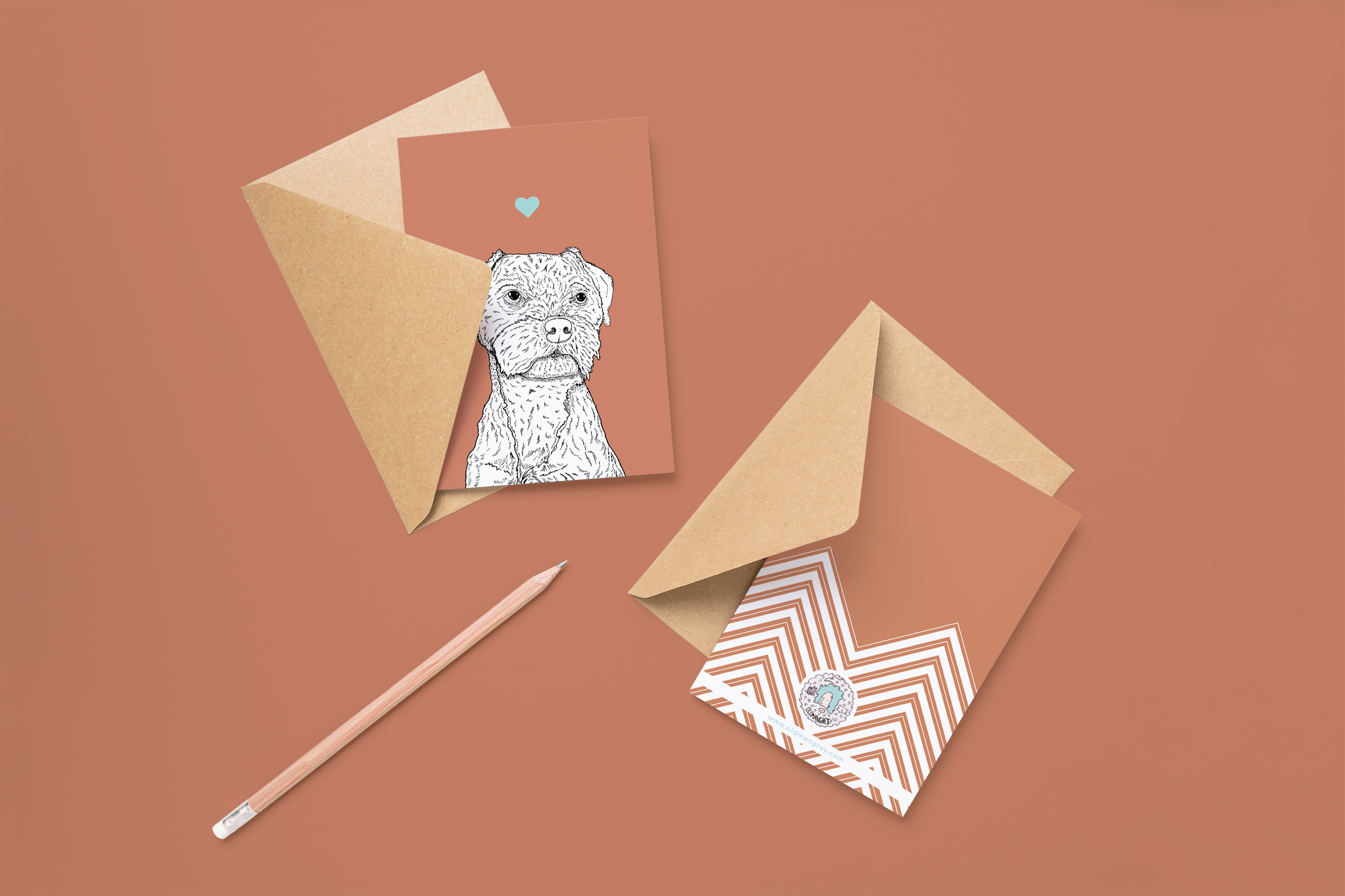 Two cards on brown envelopes, one face up one down. The card and image have a pink red coloured background, with a black & white digital illustration of the head & shoulders of a Border Terrier dog.