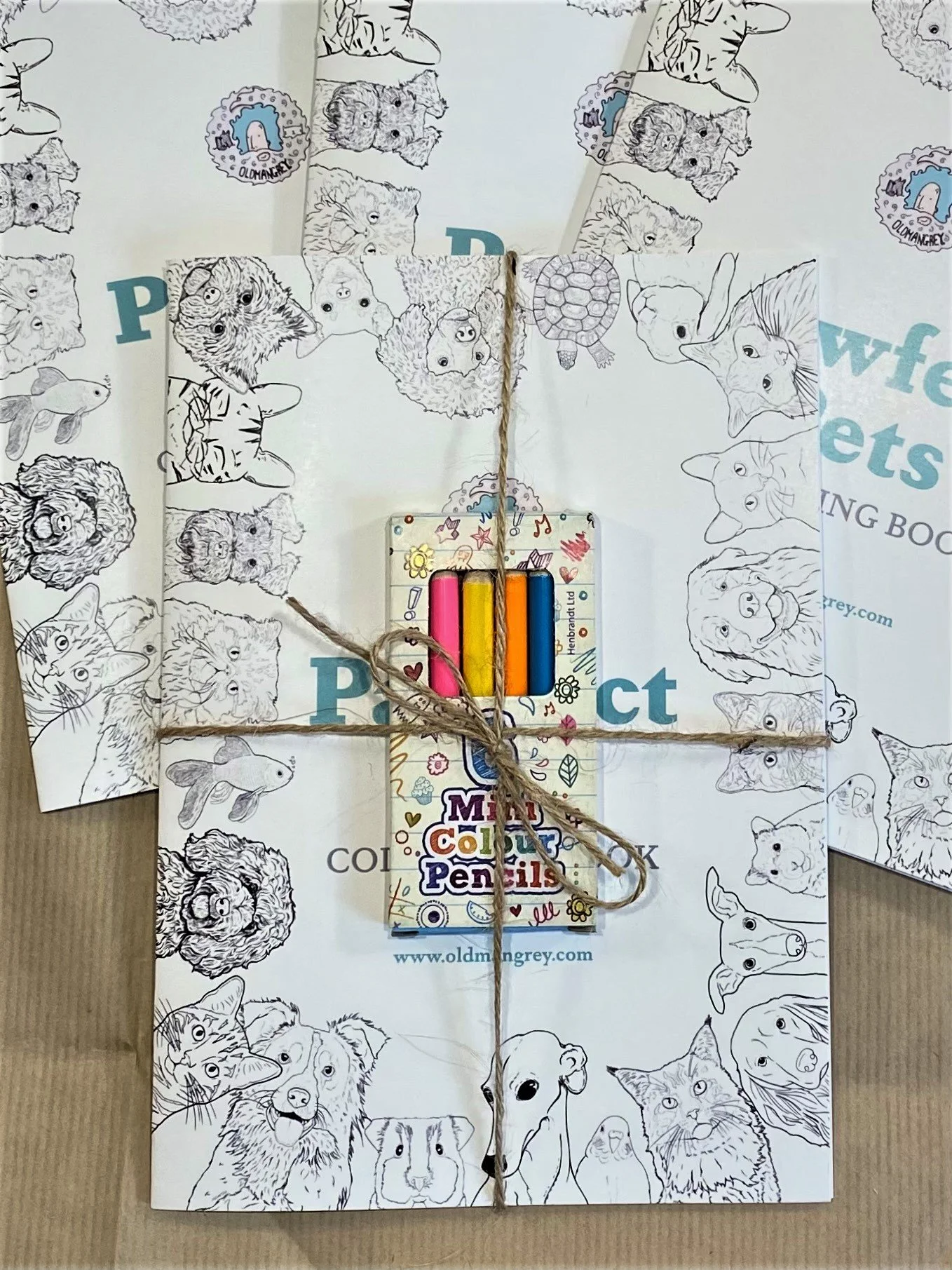 My A5 Pawfect Pets colouring book, wrapped in a string bow to tie a box of mini colouring pencils to it. Lying on fanned out copies.