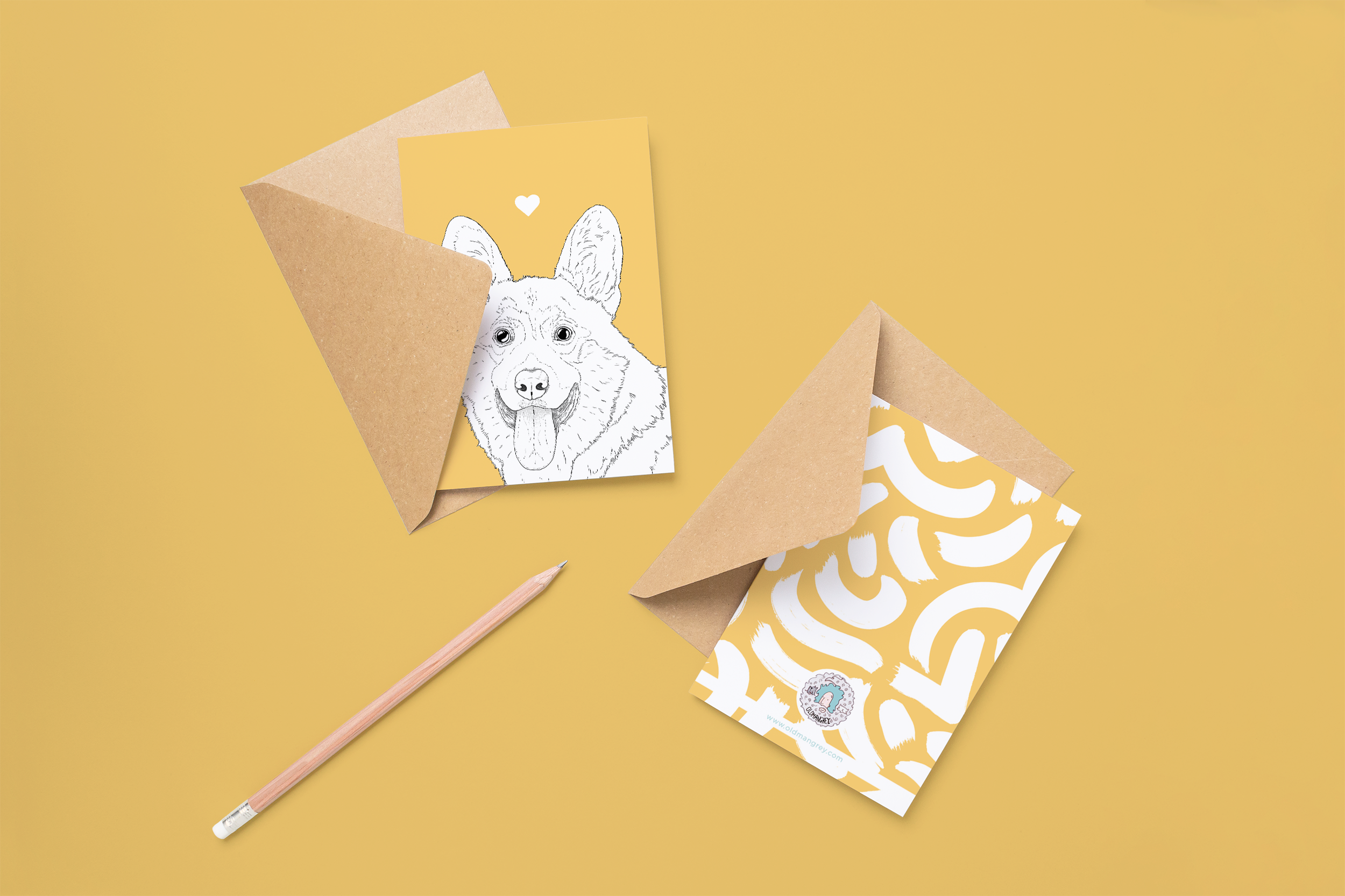 Two cards on brown envelopes, one face up one down. The card and image have a warm yellow coloured background, with a black & white digital illustration of the head & shoulders of a Corgi dog.