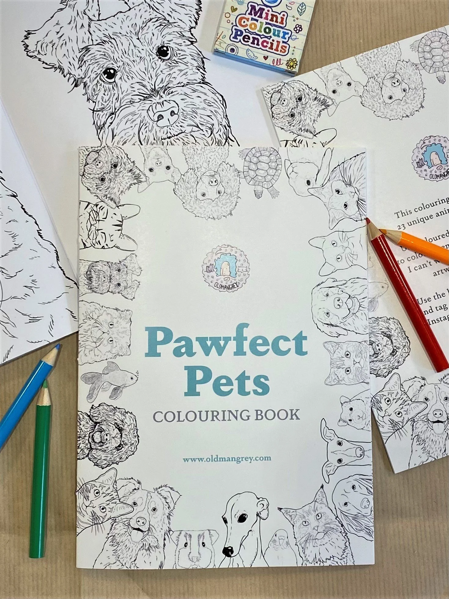 My A5 Pawfect Pets colouring book, lying on fanned out copies, with mini colouring pencils scattered around.