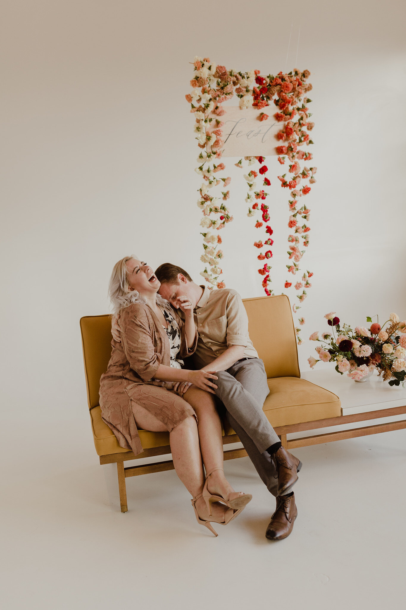 couple posing in front of photo wall with hanging floral back drop.jpg