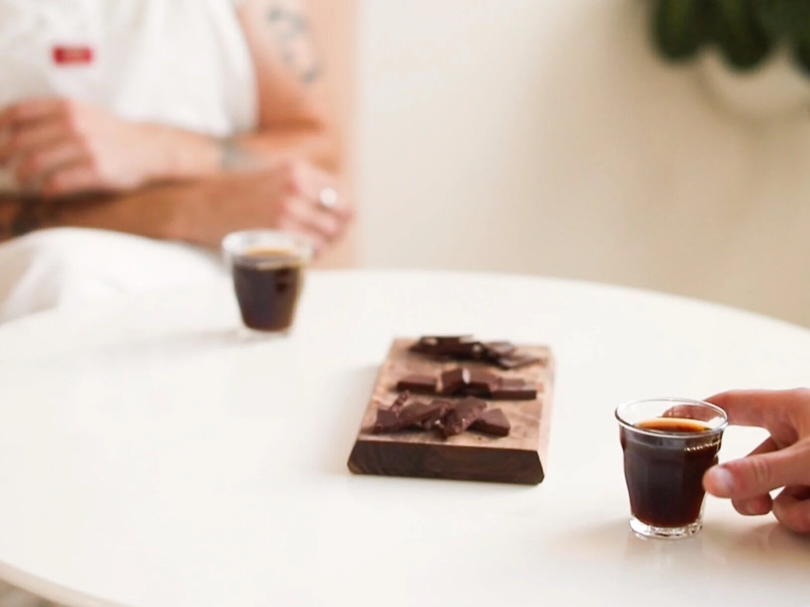 chocolate pieces on wood board on white table between two small glasses coffee