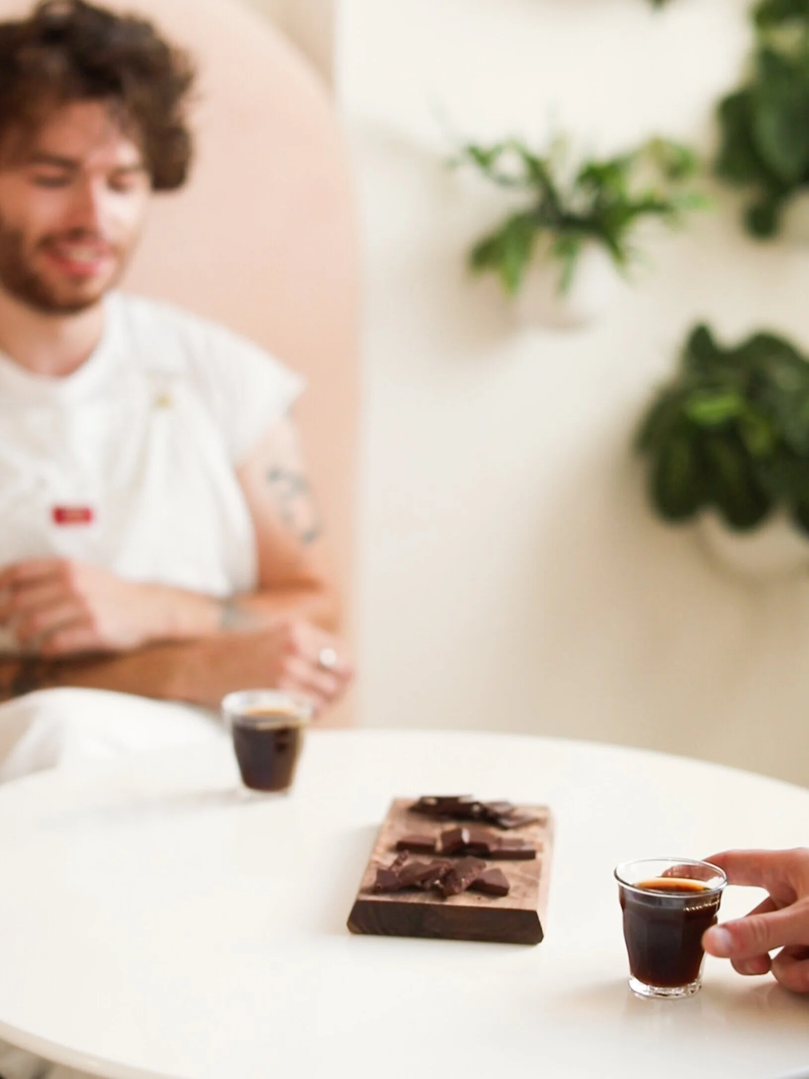 two men share chocolate pieces on wood board on white table between two small glasses coffee