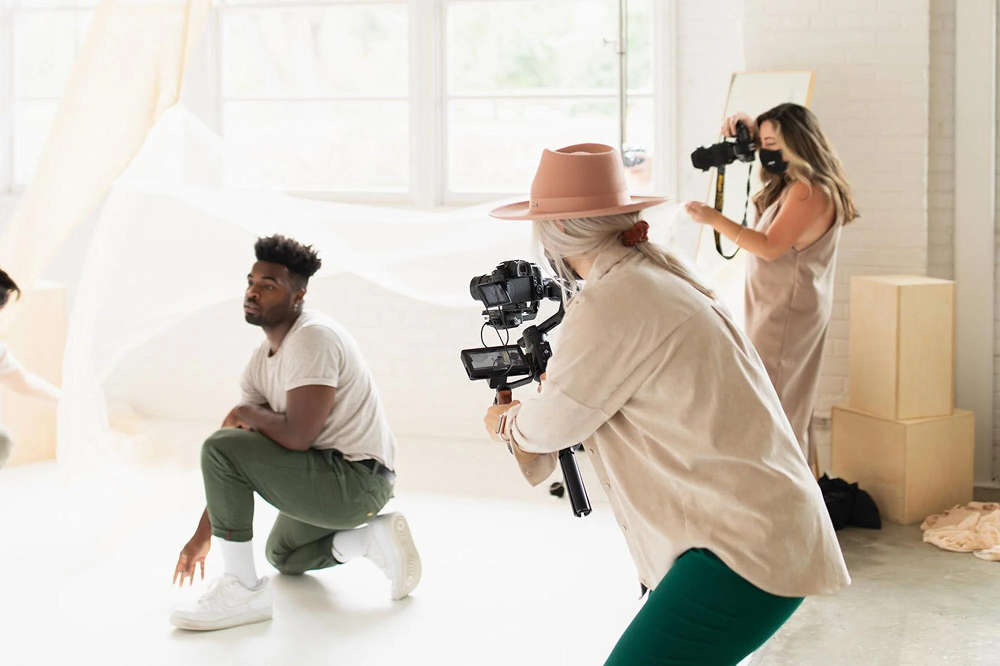Videographer and photographer shoot dancer with sheer drapes on cove natural-light cyc wall in white-walled wear-house Realm Open Space