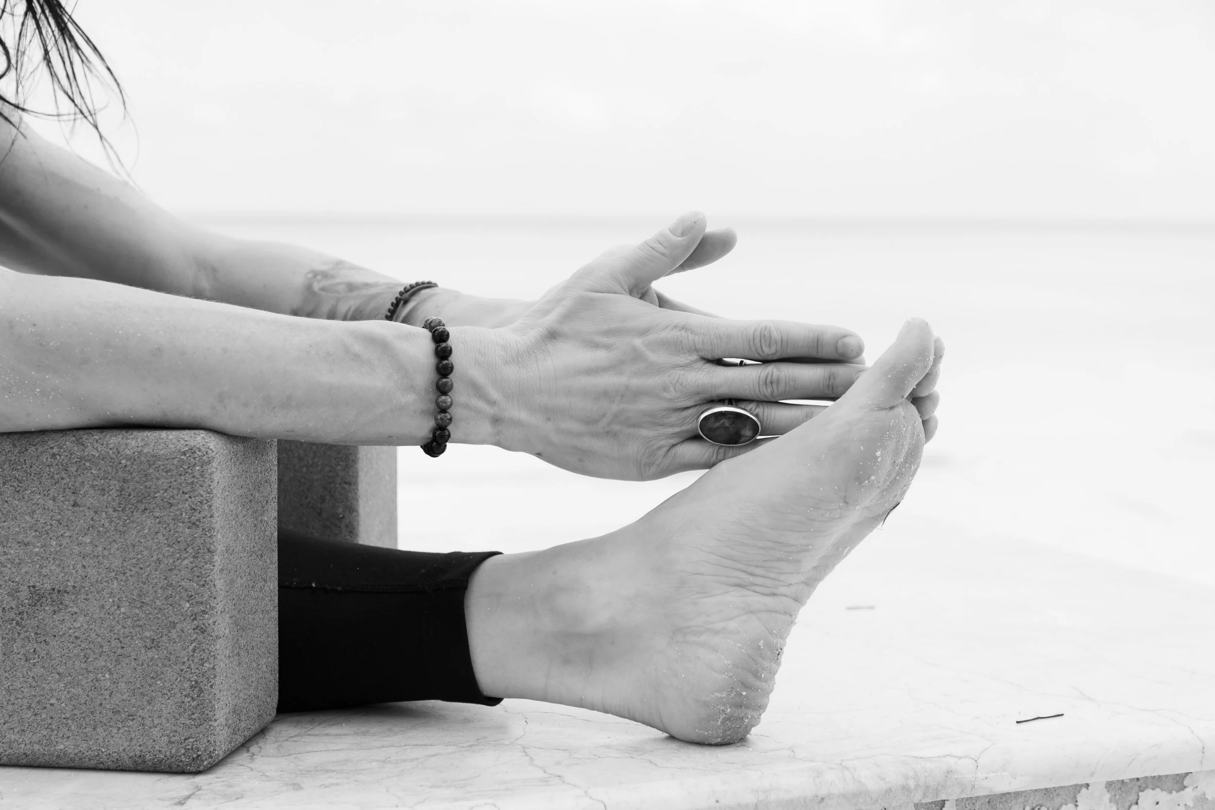 A person practicing yoga or meditation, with their feet flat on the ground and hands in a prayer or namaste position, on a textured surface with a concrete block beside them.