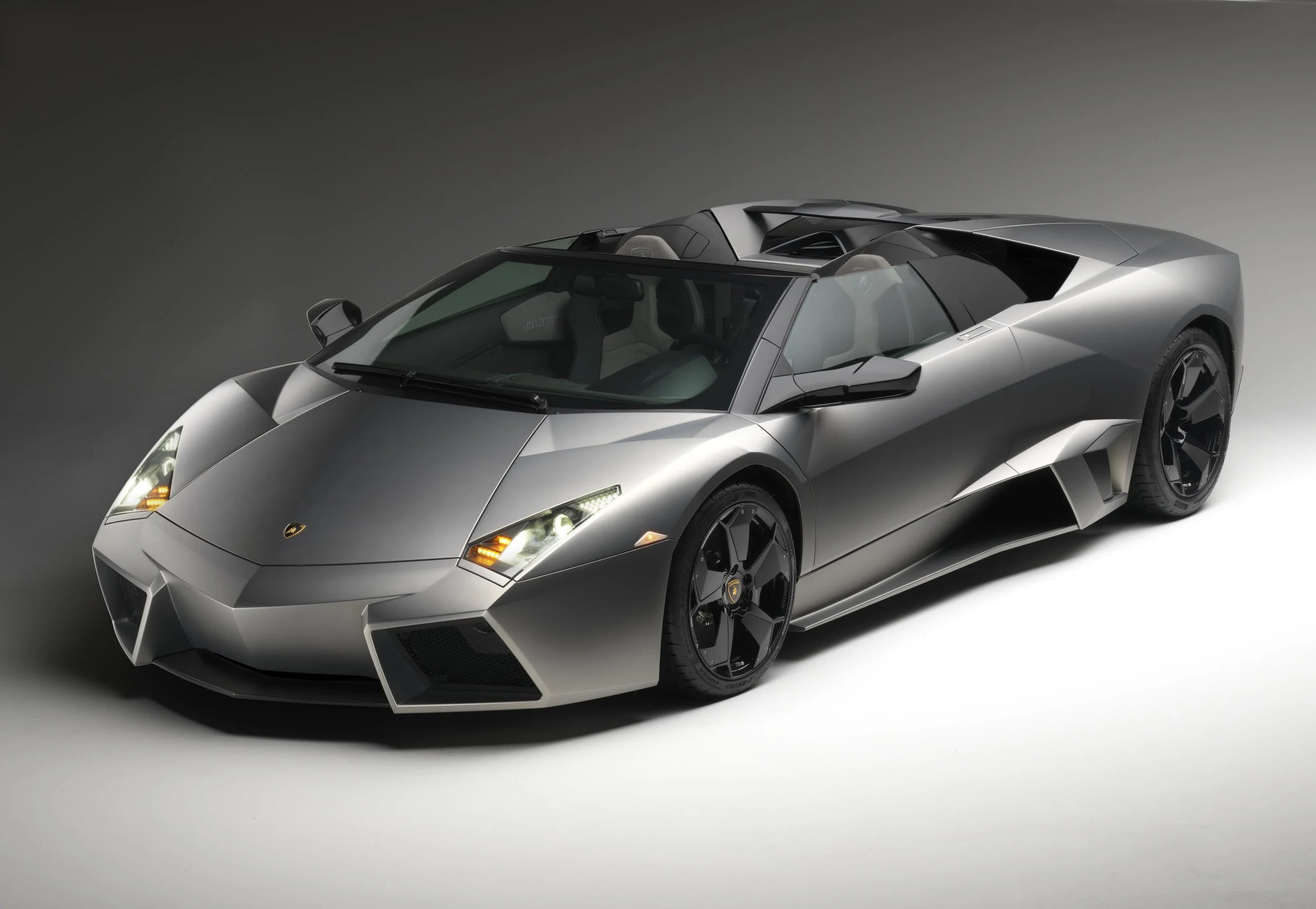 Silver luxury sports car with black accents and angular design, positioned against a plain dark background.