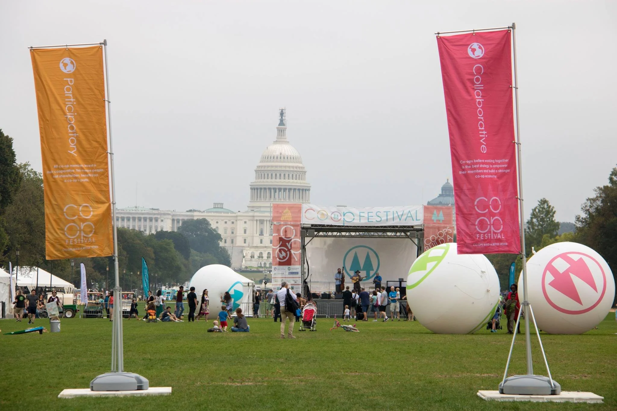 Crowd attending a festival in front of the U.S. Capitol, with stage and entertainment, colorful banners, and large decorated spheres.