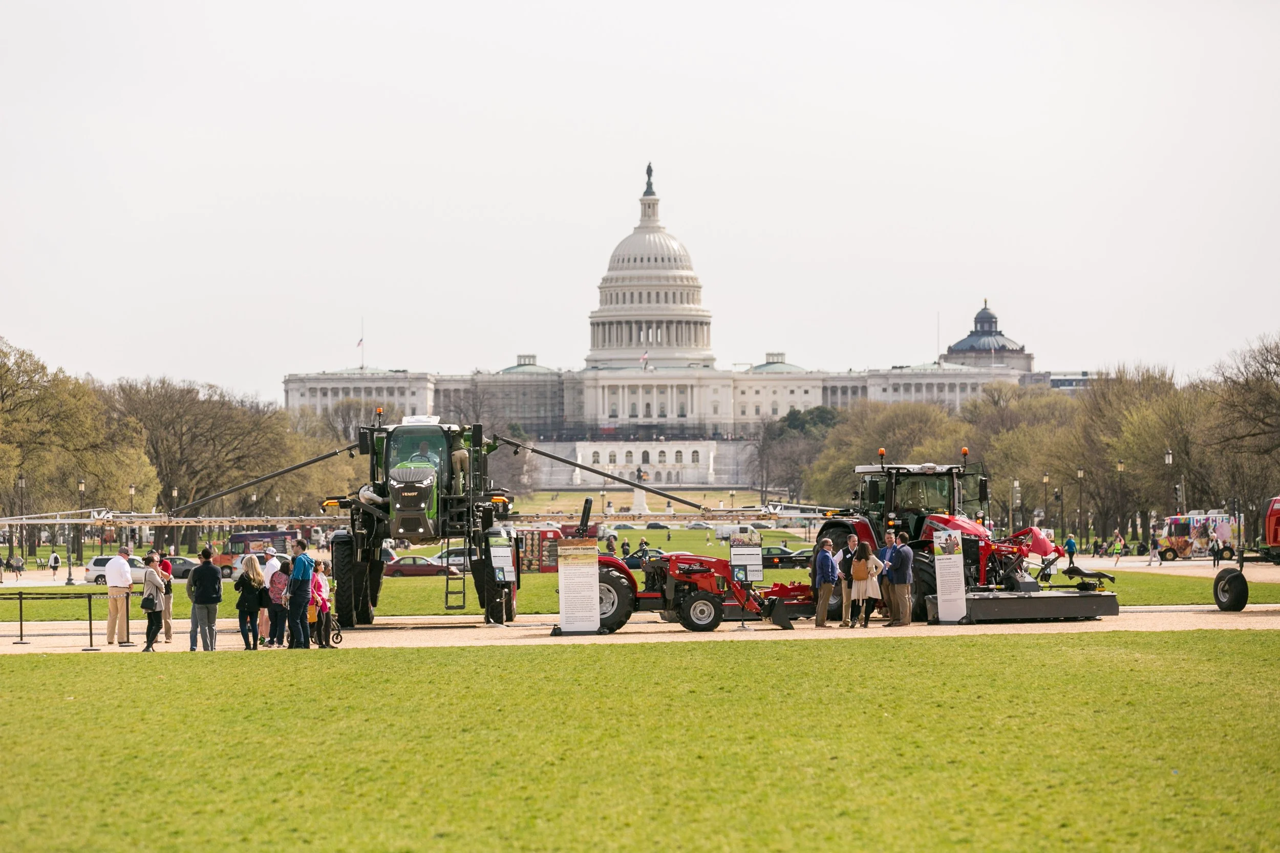 Large farming equipment and tractors on display during a festival on the National Mall in front of the U.S. Capitol, with a group of people viewing the machinery.