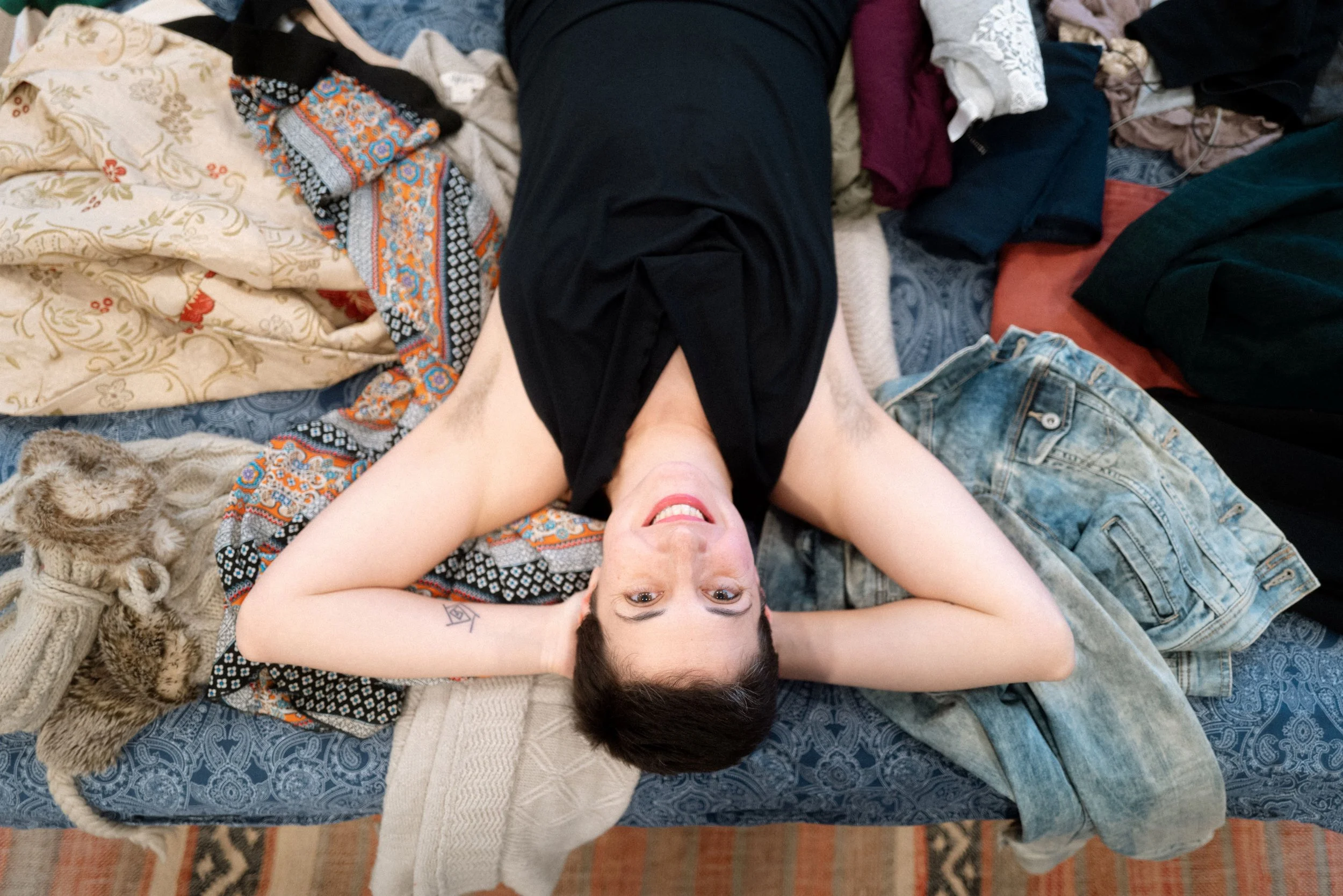 Tam laying among a pile of clothing to normalize mess and the challenges of decluttering and home organization in Nyack NY.