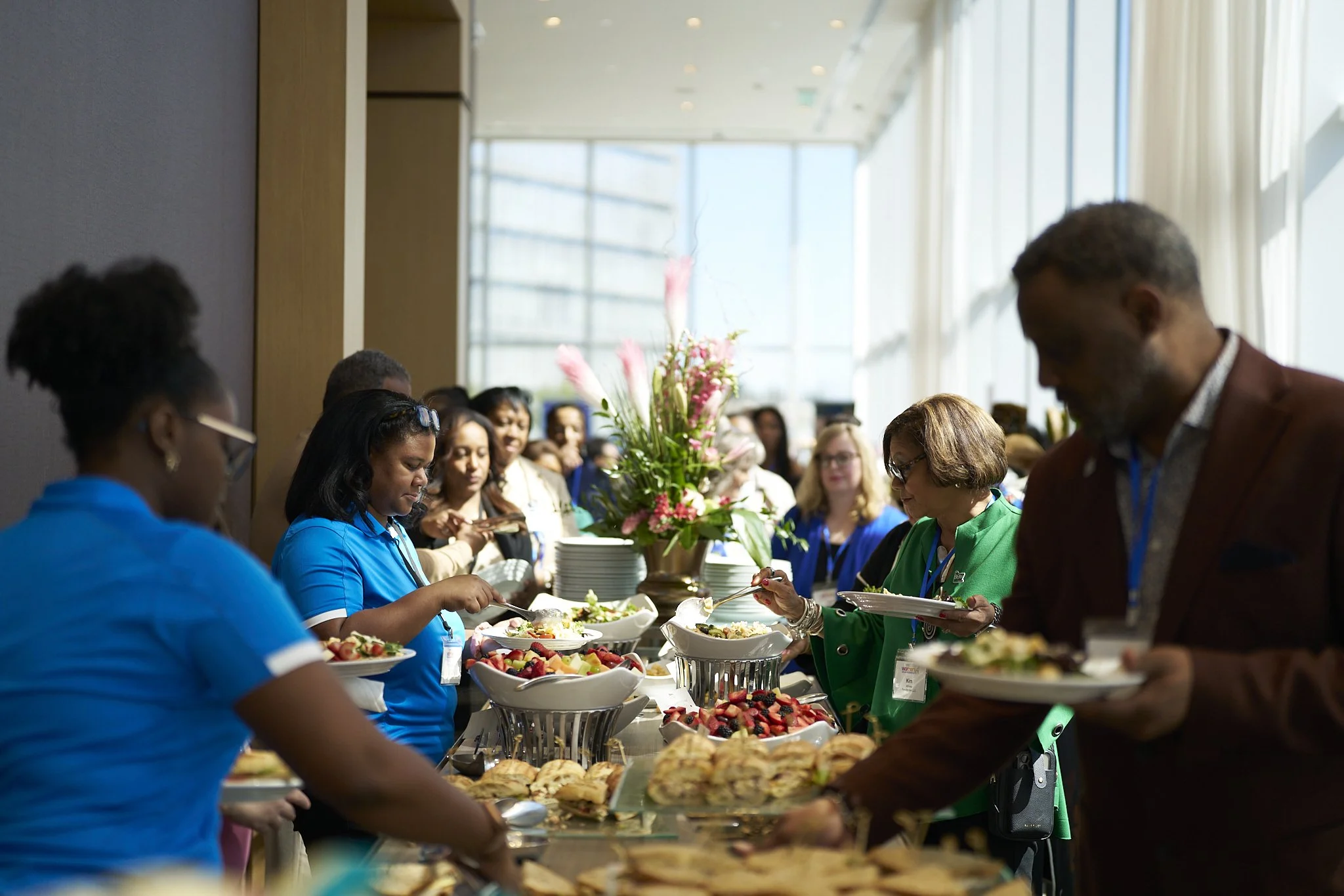 People serving themselves food at a buffet table during an indoor event. Women Mean Business. WBEC NY.
