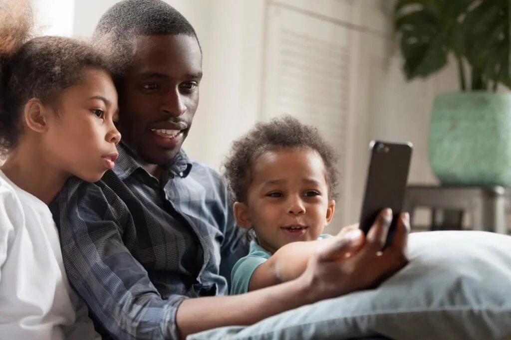 a dad looks at a phone with his daughter and son as they engage and laugh together