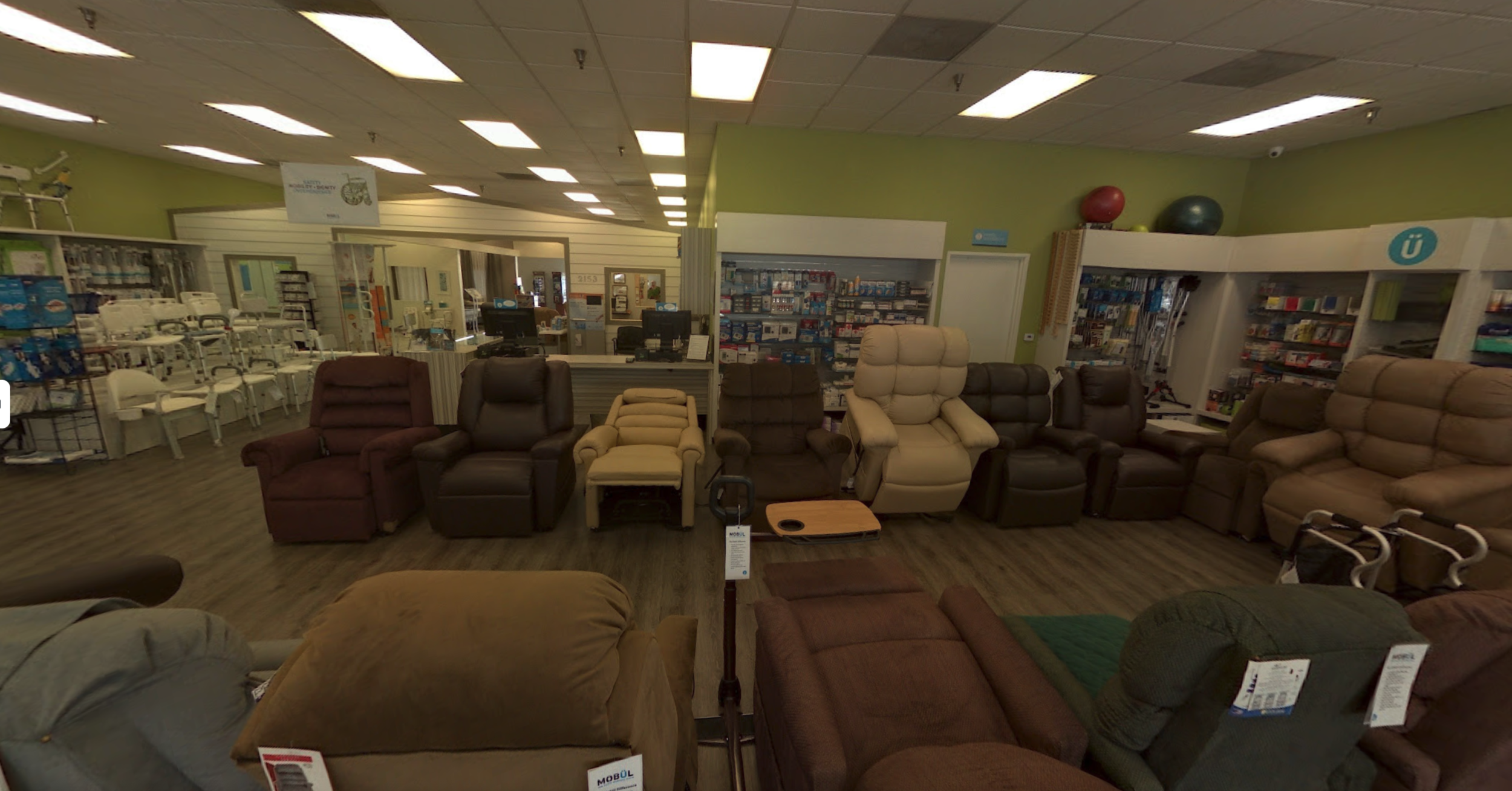 Display of various recliner chairs in a store with green walls and ceiling lights.