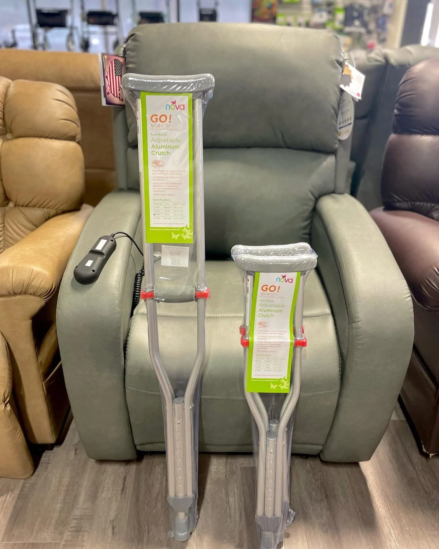 Two adjustable aluminum crutches with green and white labels, leaning against a green upholstered armchair in a furniture store.