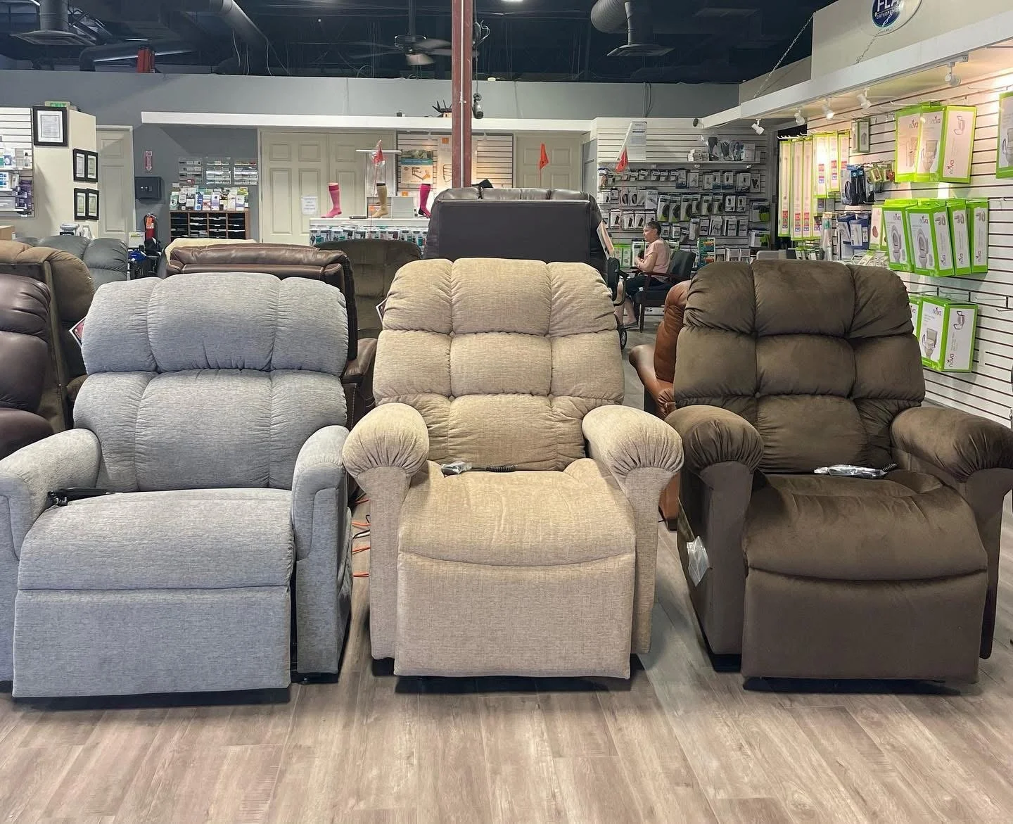 Row of three upholstered armchairs in a furniture store, with shelves of various products and a customer sitting in the background.