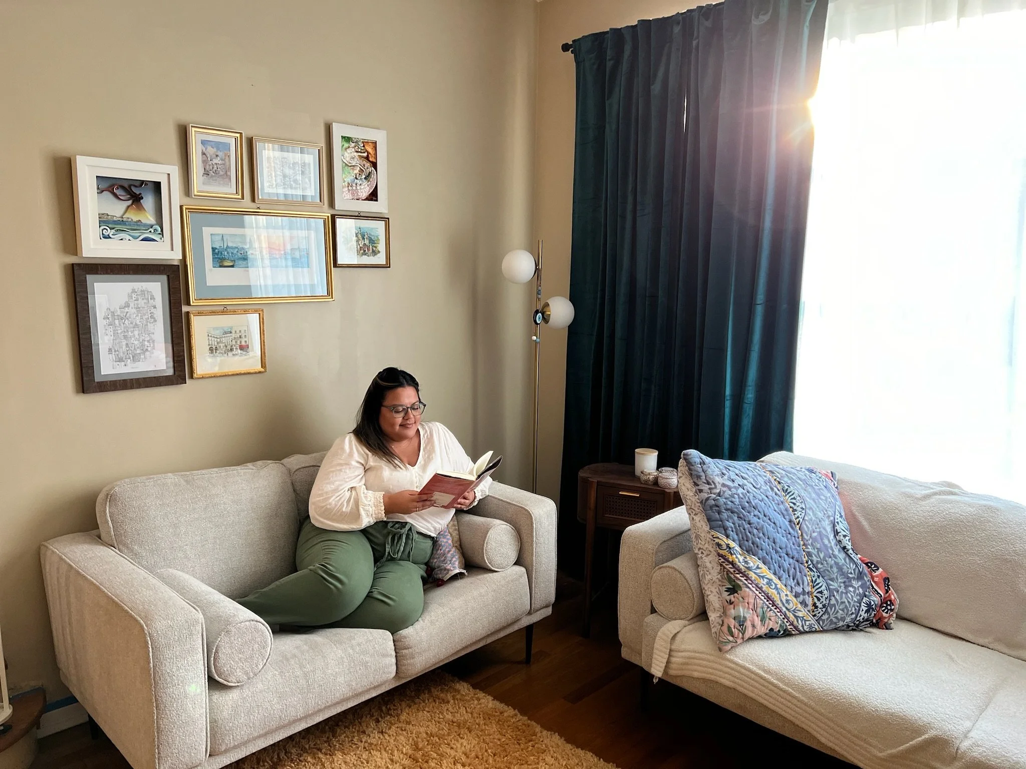A photo of Stephanie, a brown-skin, dark-haired woman, sitting on a couch reading a book.