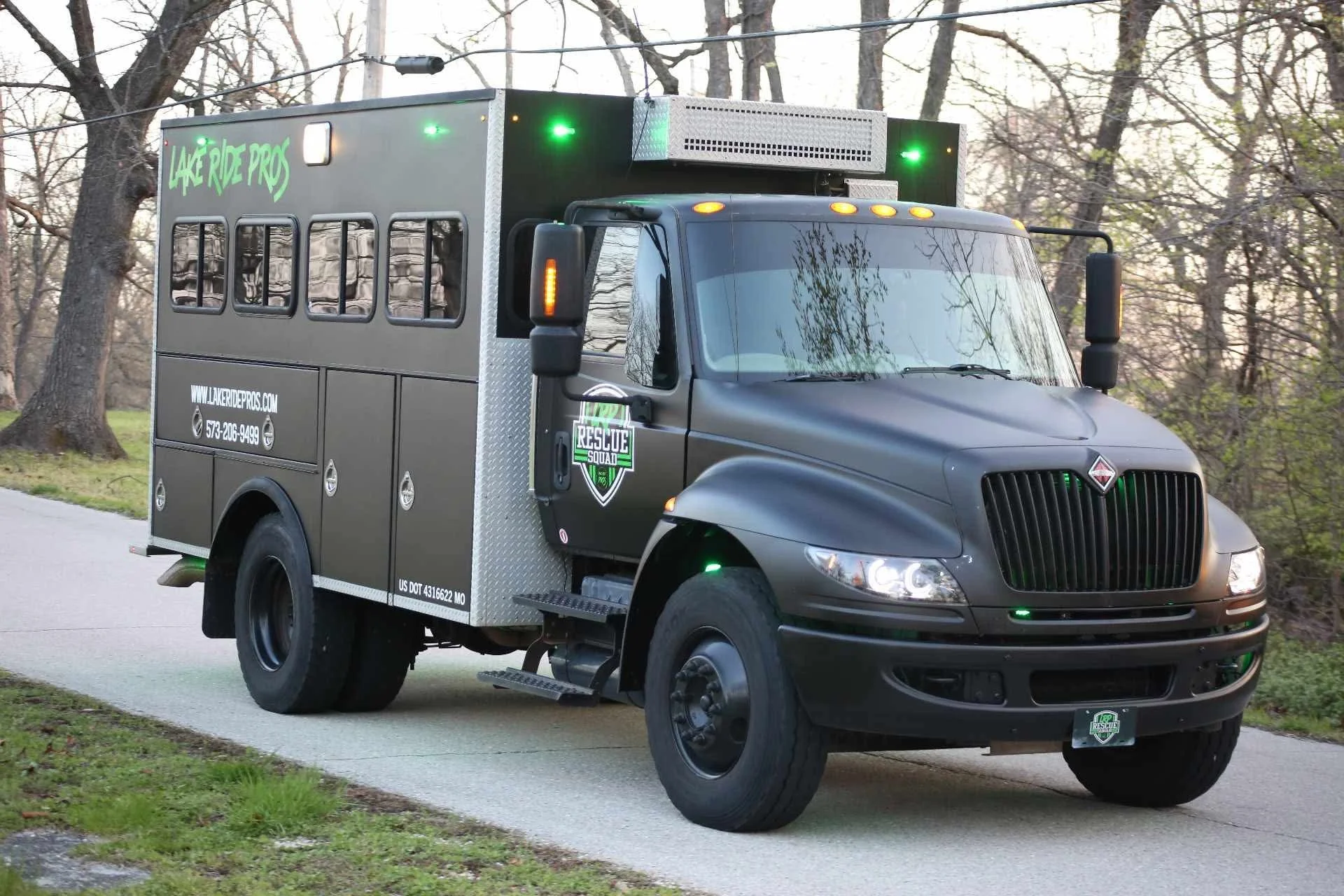 Black emergency rescue vehicle with 'Rescue Squad' and 'Lake Ride Pros' logos, parked on a paved pathway, surrounded by leafless trees and grass.
