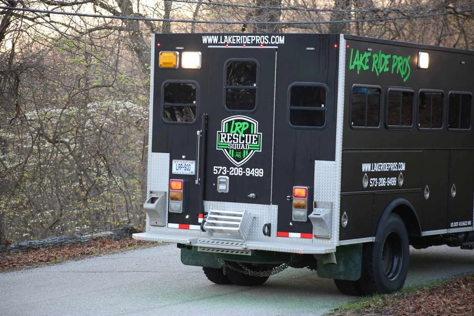 Black rescue vehicle with color green and white accents, parked on a paved road near trees, displaying website, phone number, and rescue team logo.