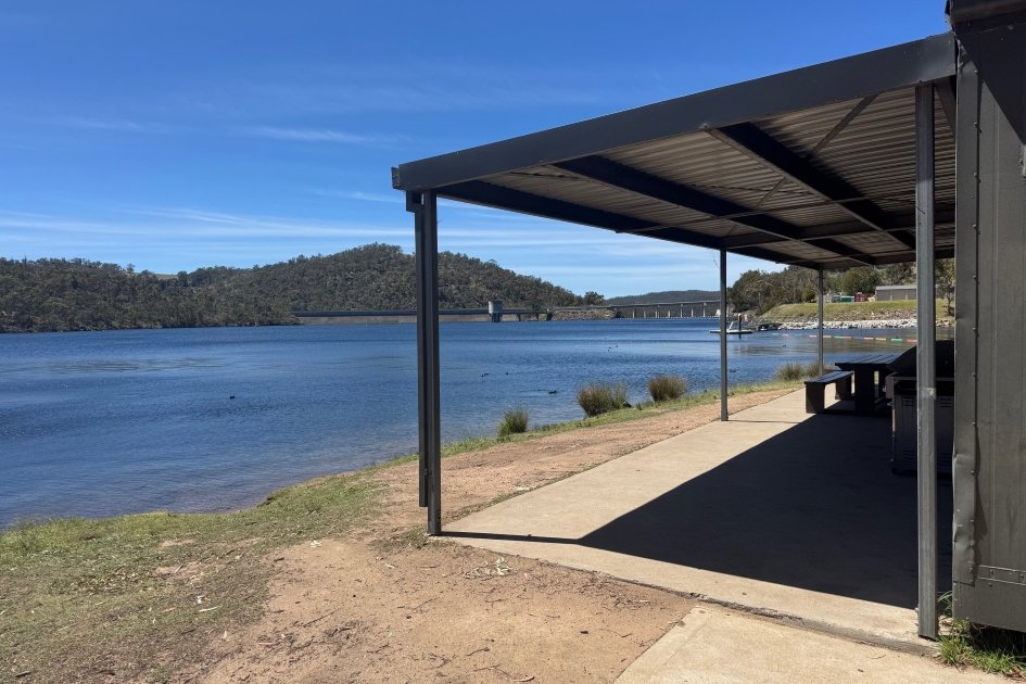 A grey roofed building and concrete flooring faces out to the blue water of a lake.