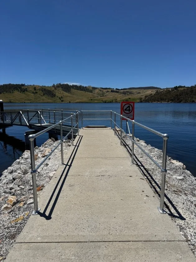 A grey concrete path with silver metal handrails leads out to the blue water