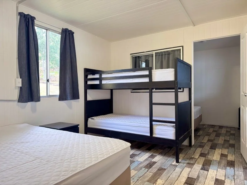 A black bunk bed with two single beds and a brown-white double ensemble feature in the second bedroom, with a blue-grey curtained window bringing light into the room.