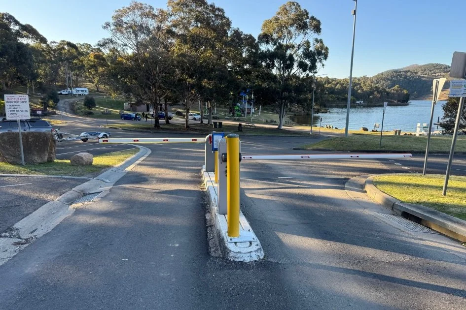 A bright yellow marker and white traffic island stand at the front of  two horizontal white boom gate poles