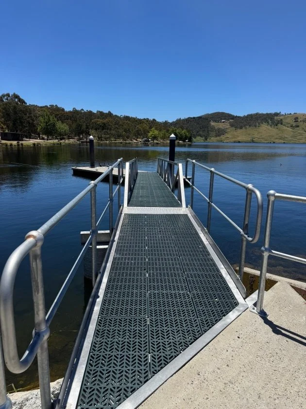 A grey mesh path with silver metal handrails leads out to the blue water