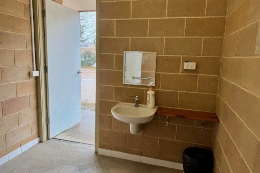 A large white door is open to outside with a wall mounted white porcelain sink and mirror  positioned to the right