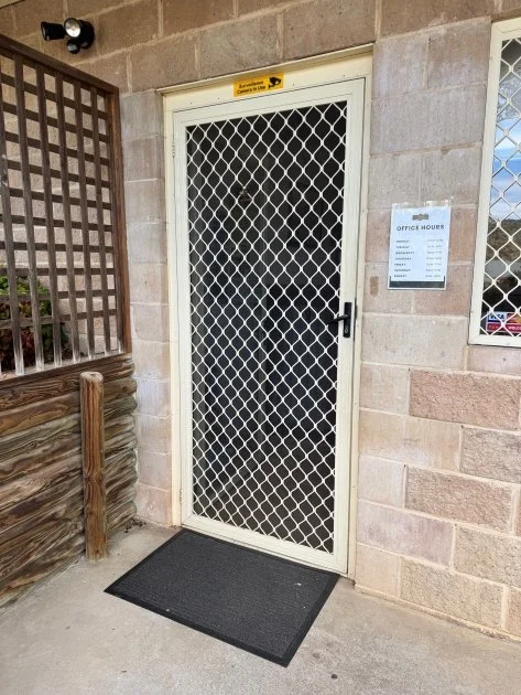 A vertical cream coloured screen door  with a black and grey door mat and timber screening to the left