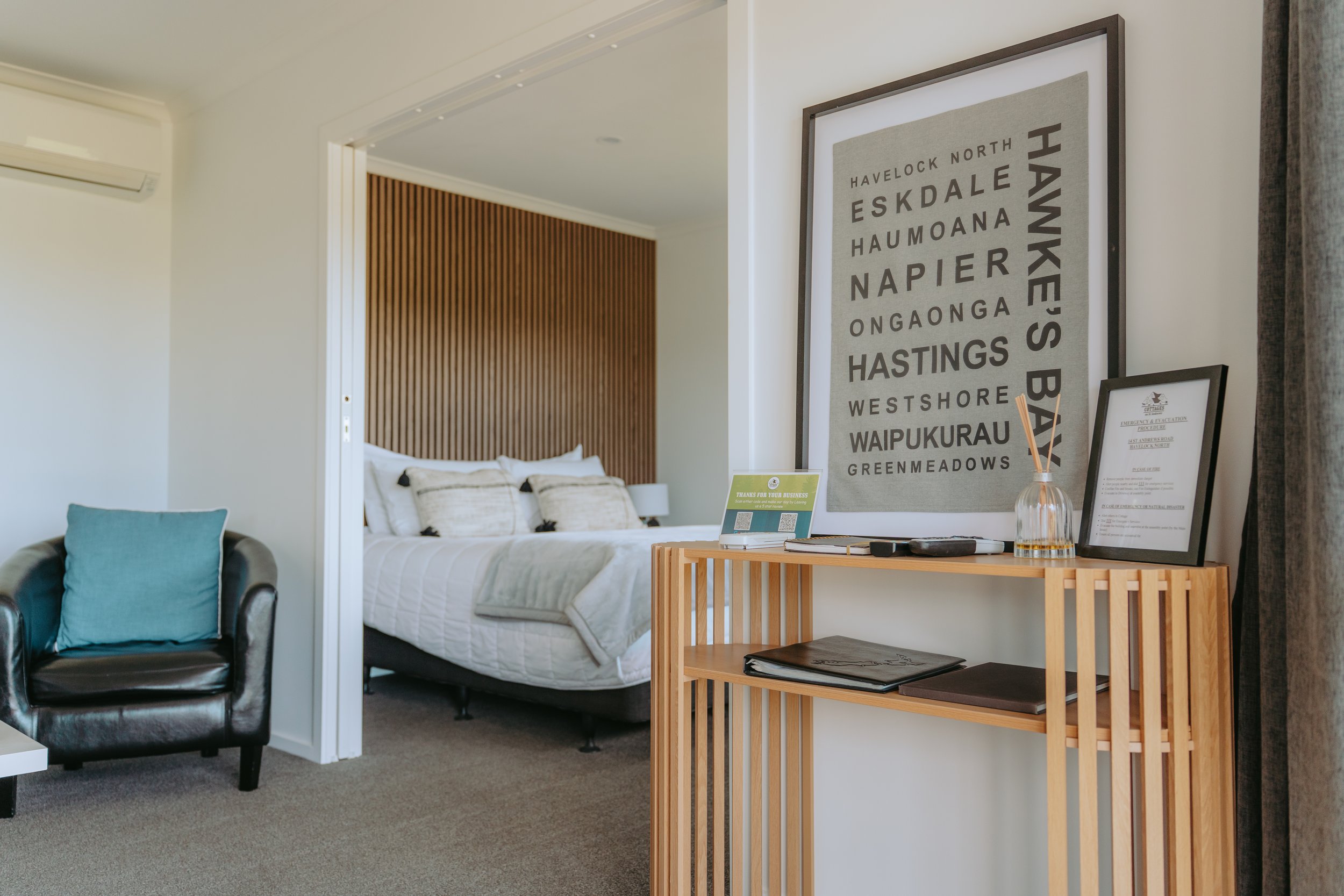 Living room with leather sofa, armchair, black and wooden rocking chair, white coffee table, window view of green yard, and wall art of two goose necks.