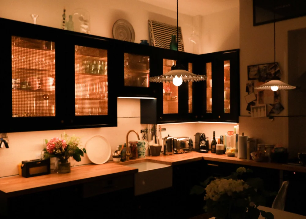 The rattan-filled kitchen cabinets lit up at night. The pendant lamps are from Retrouvius