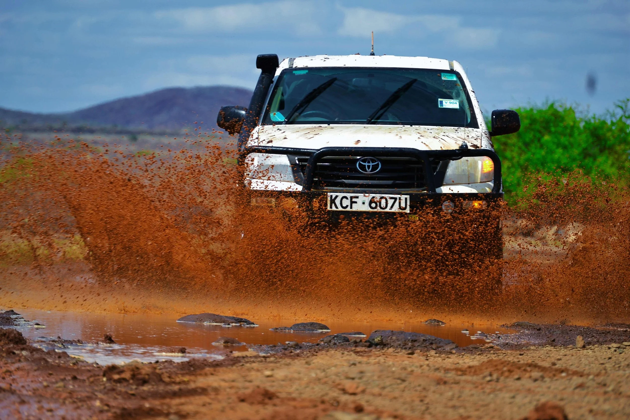 A tan off-road SUV navigating rocky terrain with orange traffic cones marking the path in a desert landscape.