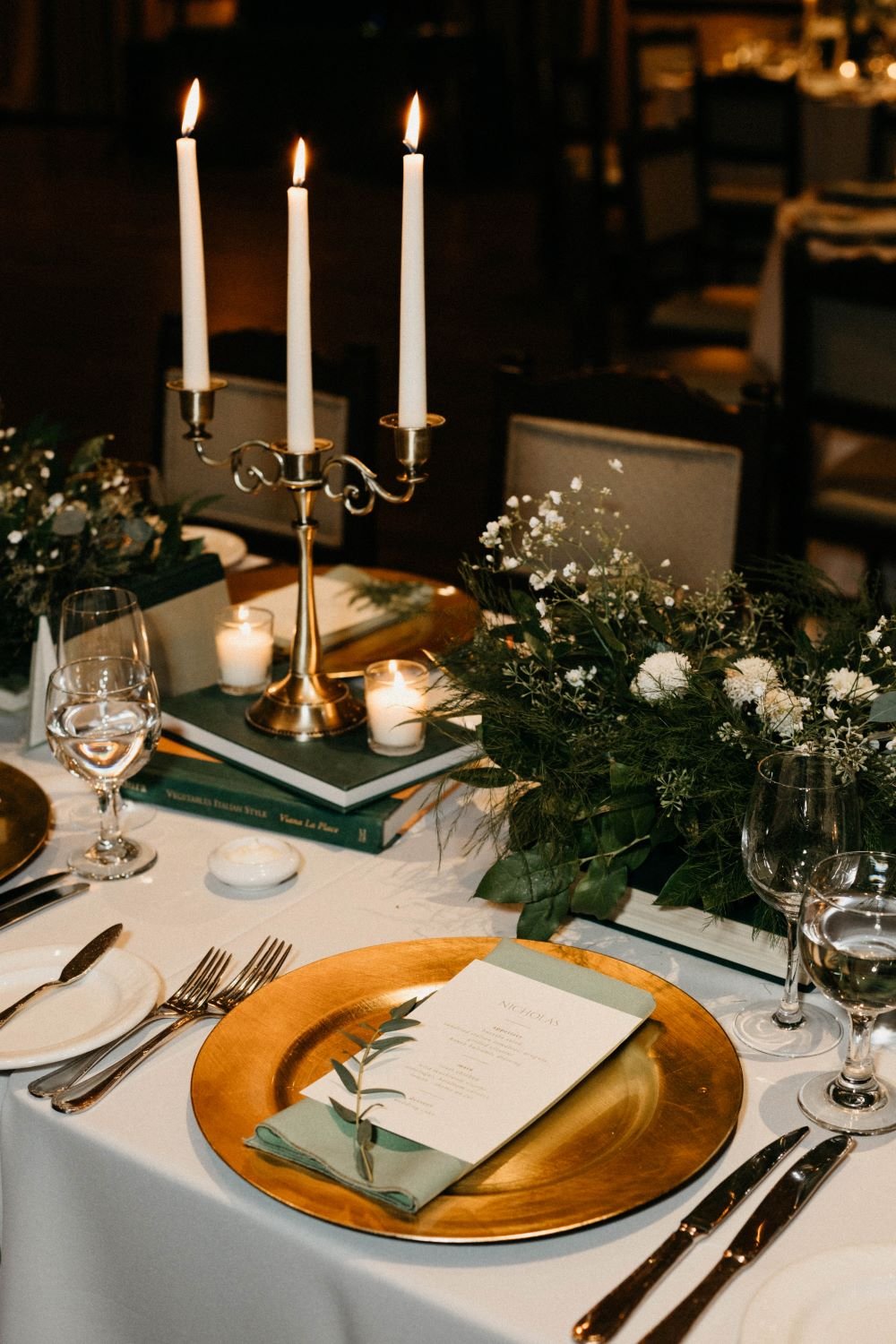 How to give a great wedding rehearsal toast speech, flowers and candles sit on a table adorned with books, a gold plate and personalized menu, let's get rehearsed