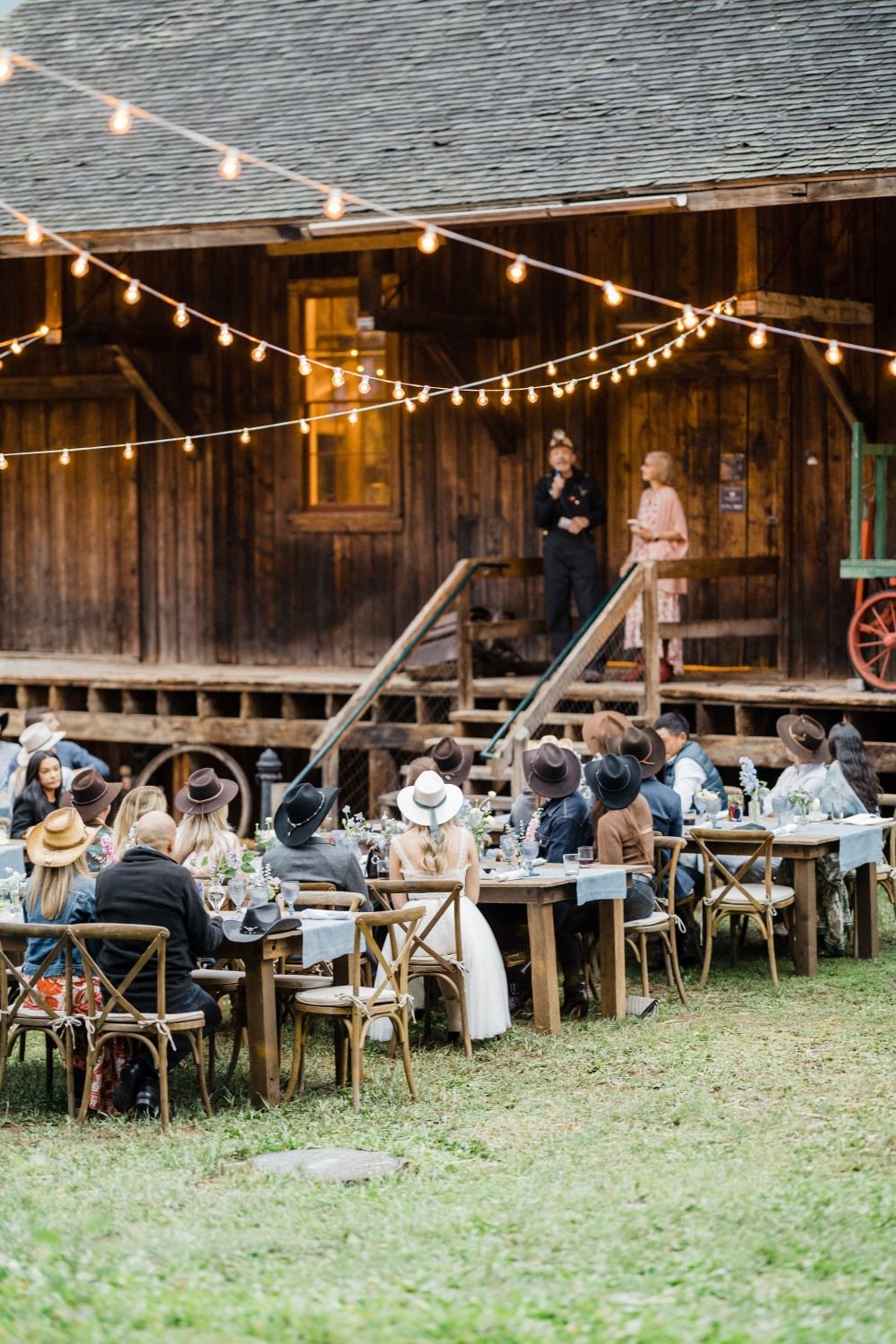 Tips and tricks for giving a wedding rehearsal dinner toast, wedding guests & bride & groom in cowboy hats sit watching a couple give a wedding rehearsal toast, let's get rehearsed