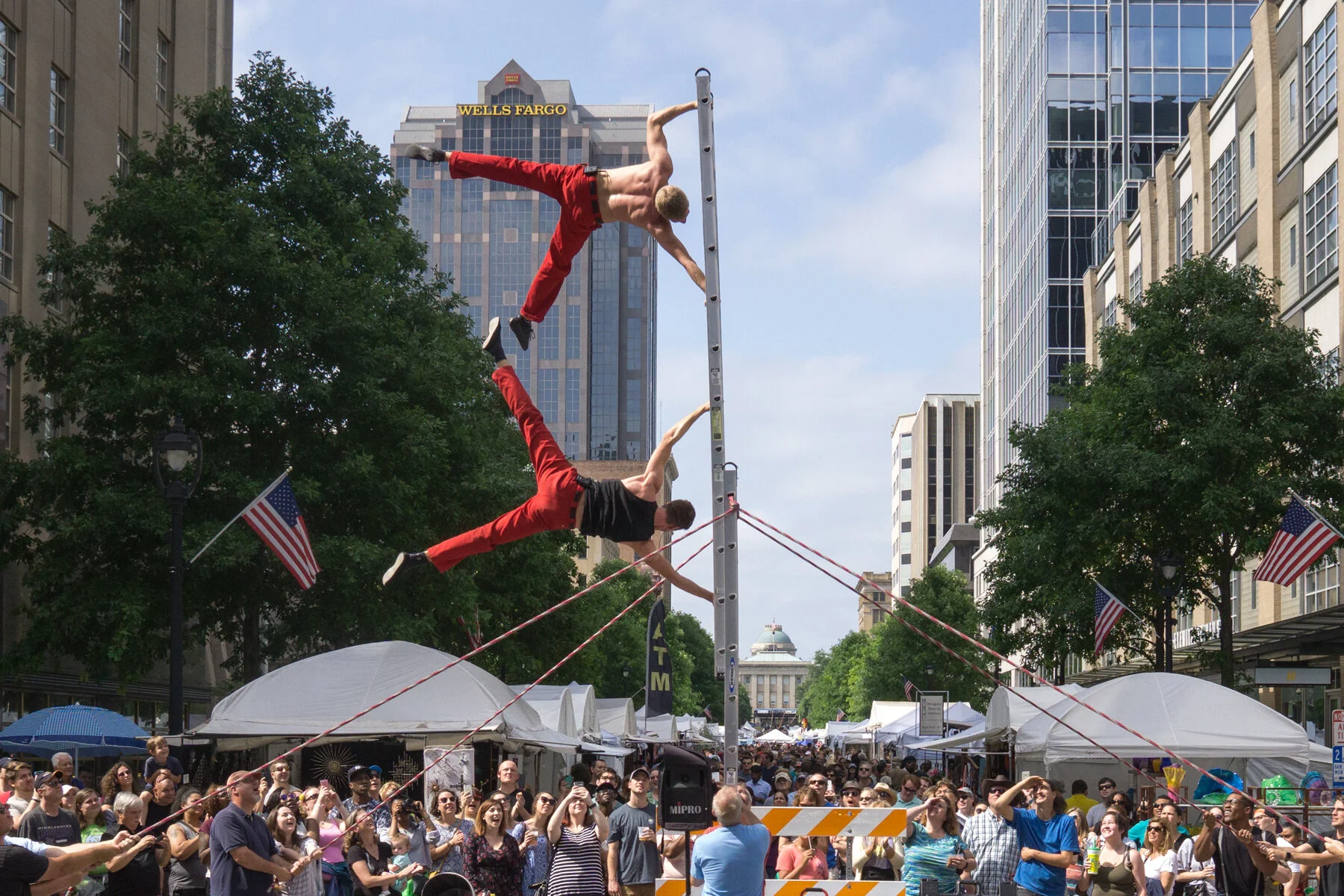  Two acrobatic street performers holding onto a pole above a large crowd on Fayetteville Street in downtown Raleigh at the Artsplosure - Raleigh Arts festival 