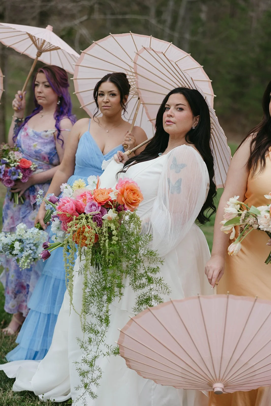 Women standing outdoors holding floral bouquets and pink umbrellas