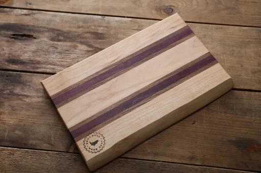 Commissioned maple cutting board with purple heart and walnut accents and live edge on one side