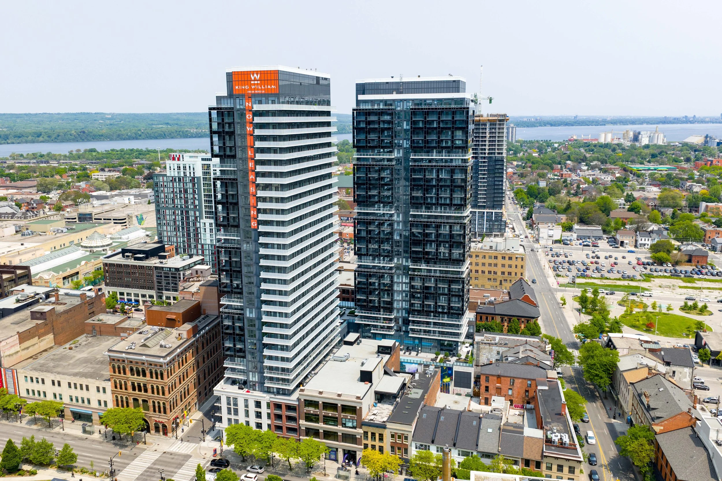 High-rise buildings in an urban landscape near a river, with trees and smaller buildings in the foreground.