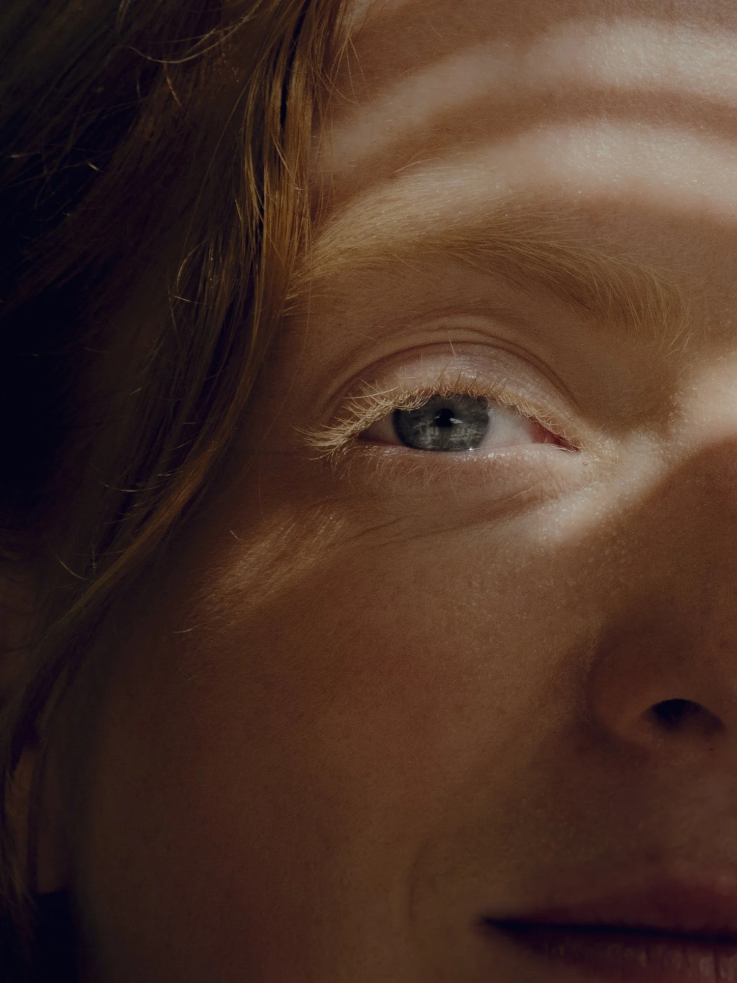 Close-up of a woman's face, focusing on her eye, nose, and part of her lips, with natural lighting and a slight smile.