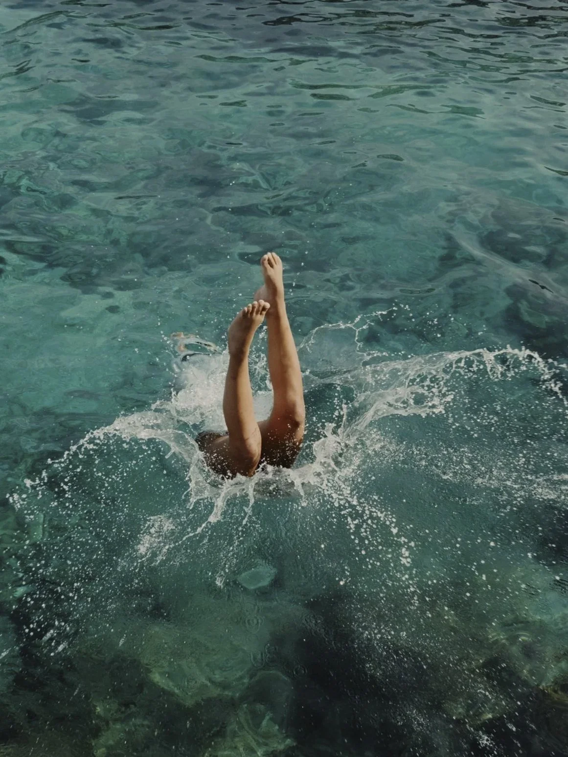 Person diving into clear blue water, with legs and feet visible above the water surface.