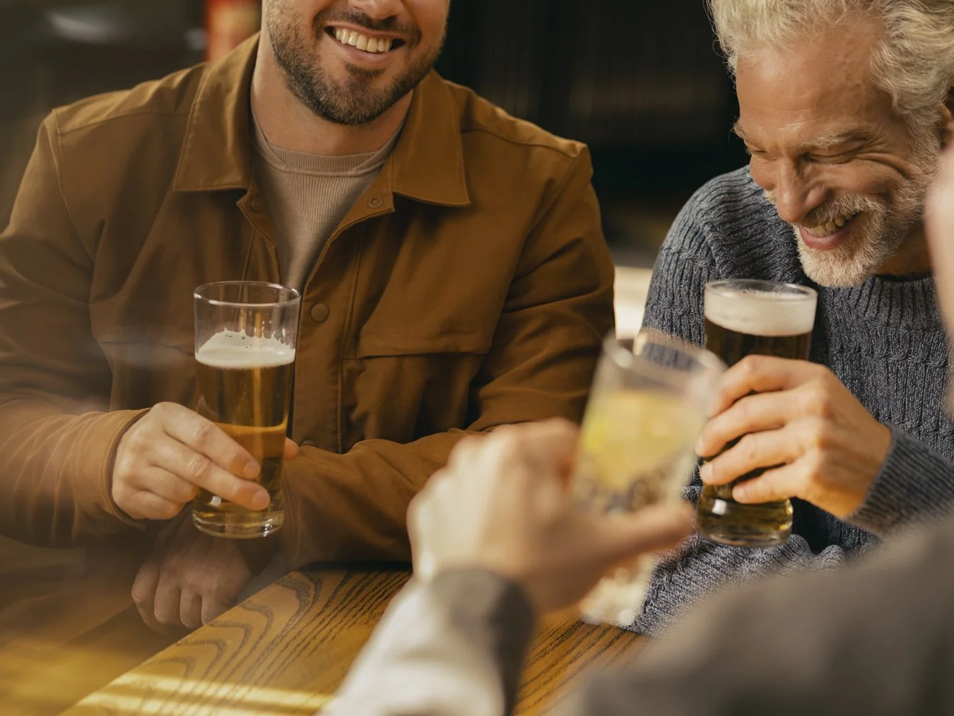 Three men enjoying drinks and socializing at a bar, smiling and holding glasses of beer.