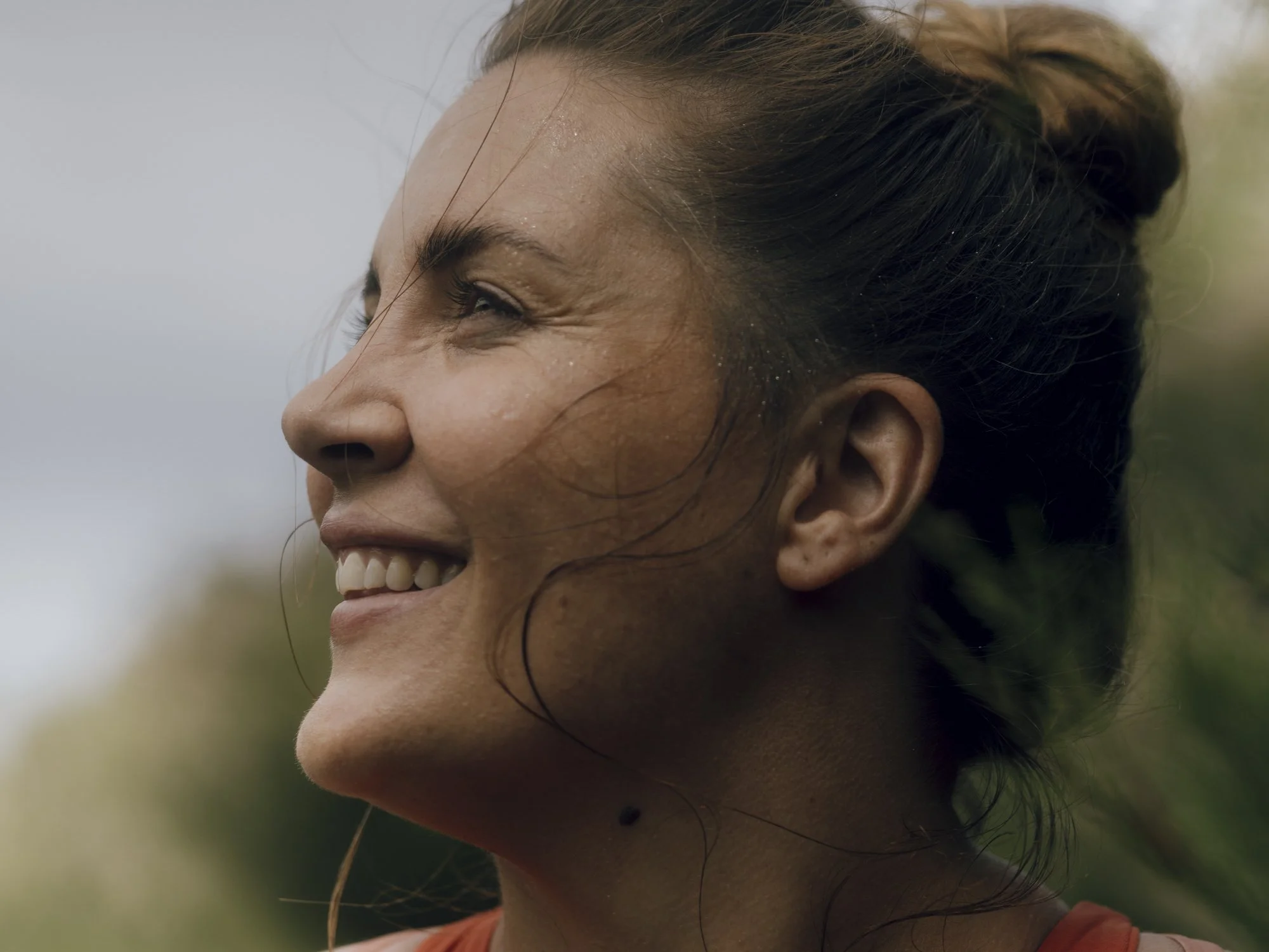 A smiling woman with freckles and a bun hairstyle enjoying an outdoor moment.