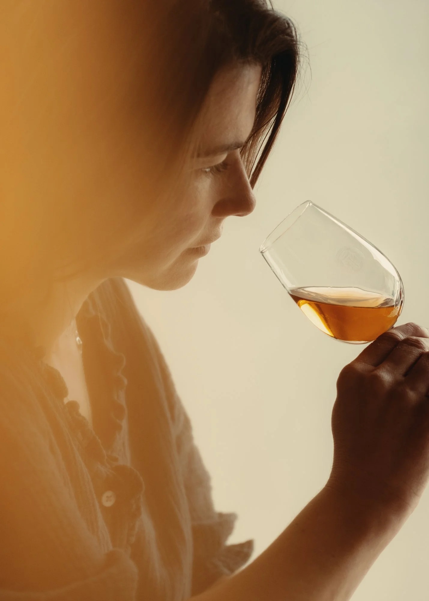A woman inspecting a glass of amber-colored liquid, likely whiskey or bourbon.