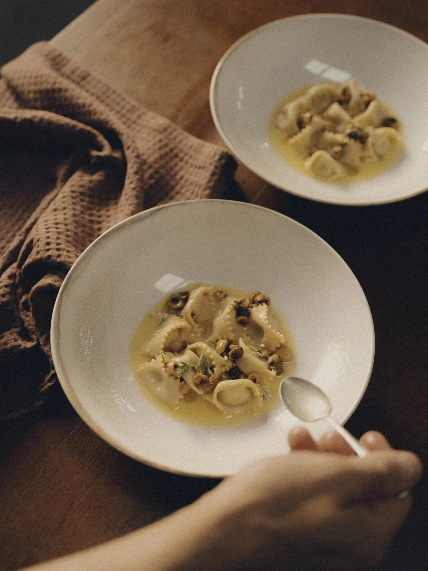 Two white bowls of pasta with sauce and lentils, placed on a wooden table with a brown cloth in the background.